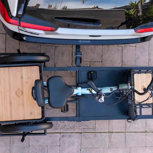 Electric trike securely mounted on a rear hitch rack behind a parked car, viewed from above.