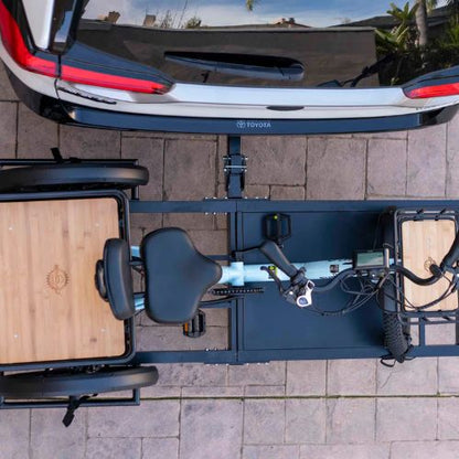 Electric trike securely mounted on a rear hitch rack behind a parked car, viewed from above.