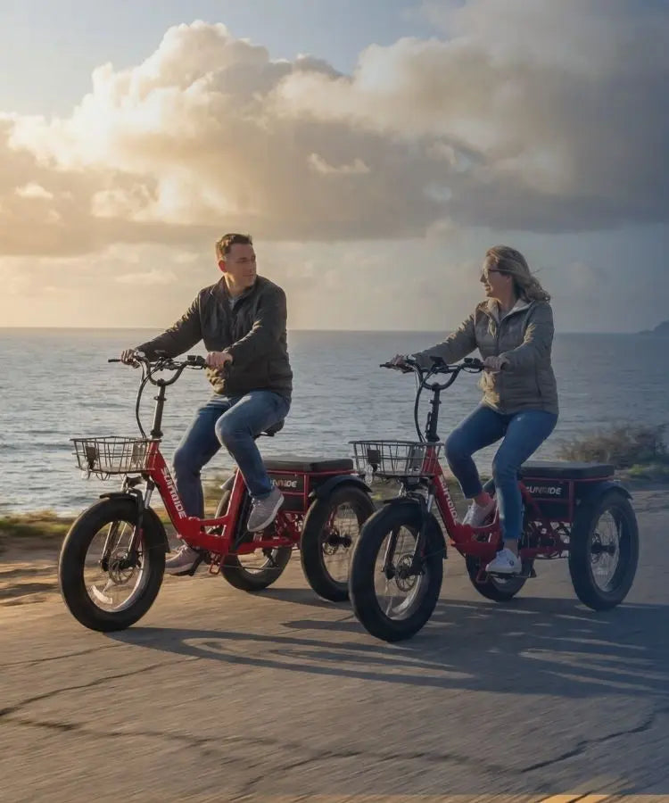 Two people riding electric trikes on a beach with a scenic ocean view.